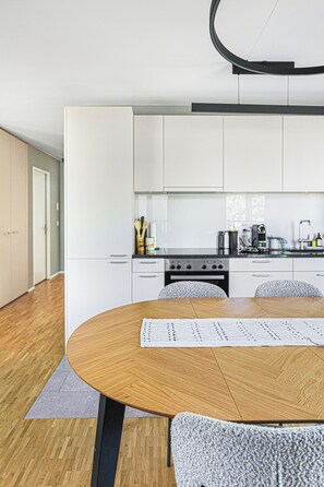 Een moderne keuken met witte kastjes, een houten eettafel en een zwart plafondarmatuur.