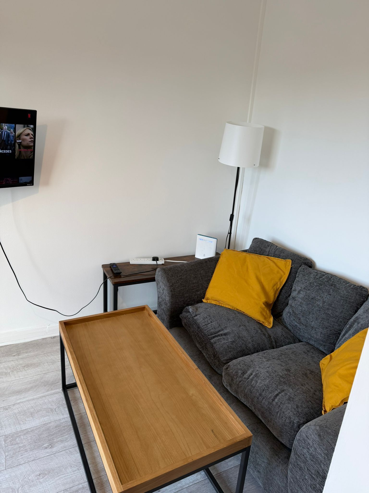 A living room with a sofa, a wooden coffee table, a lamp, and a TV mounted on the wall.