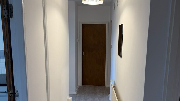 A hallway with a wooden door at the end, a ceiling light fixture, and a radiator on the wall.