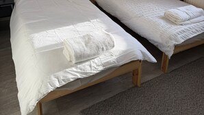 Two single beds with white bedding, a small table with a lamp, and two wall-mounted pictures.