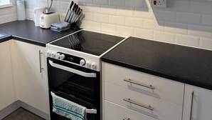 A kitchen with white cabinets, a black countertop, a stainless steel range hood, a built-in oven, and a window.