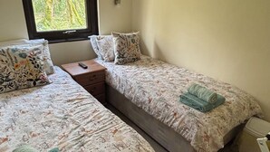 Ein Schlafzimmer mit zwei Betten, einem Fenster, einem Nachttisch und einem kleinen weißen Stuhl.