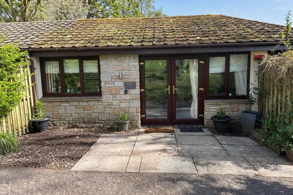 Une maison de campagne en pierre avec un toit en tuiles, une porte d’entrée en pierre et un petit porche agrémenté de plantes en pot.