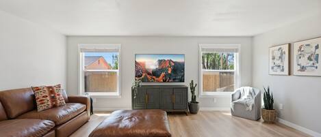 A living room with a brown leather sofa, a grey cabinet, a television, and a window with a mountain view.
