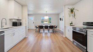 A modern kitchen with white cabinetry, a dining table with chairs, a microwave, and an oven. - Oak Haus | Group Stay w/ Fenced Yard & Game Room (Windsor)