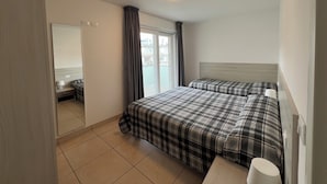 A hotel room with a bed, a mirror, a window with curtains, and a ceiling light.