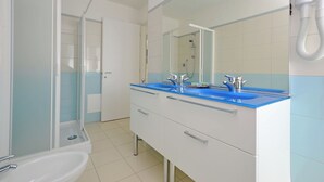 A bathroom with a shower, two sinks, a mirror, and a towel rack.