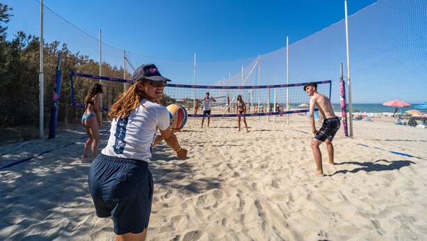 Ein Beachvolleyballspiel auf einem Sandplatz mit Netz, umgeben von einem Zaun.