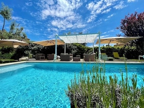 A swimming pool with lounge chairs and umbrellas, surrounded by greenery. - The Gîte Ventoux story (Bédoin)