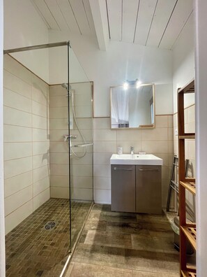 A bathroom with a glass shower enclosure, a sink with a mirror above it, and a wooden floor. - The Gîte Ventoux story (Bédoin)
