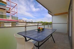 Un balcon avec une table et des chaises, un saladier rempli de fruits et une vue sur les bâtiments et les arbres.