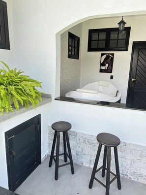 A modern outdoor seating area with a white sofa and two stools, a black door, and a decorative horse painting on the wall. - Spacious vacation home for 10 people with pool 200 meters to the beach (Niterói)