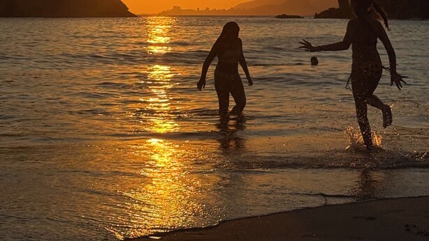 Pôr do sol sobre a água, com silhuetas de pessoas.