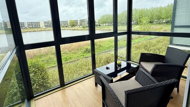 Moderni huone, jossa on suuret ikkunat, pieni pöytä ja rottingista valmistetut huonekalut.