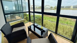 Huoneessa on suuret ikkunat, lasipöytä ja kaksi rottinkituolia.