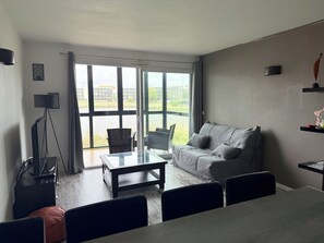 A modern living room with a sofa, a coffee table, and a TV on a tripod stand.