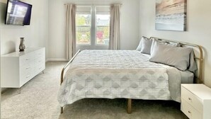 Un dormitorio con cama, televisor, cómoda y ventana con cortinas.