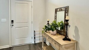 Un pasillo con una puerta blanca, una consola de madera con espejo y una planta en maceta.