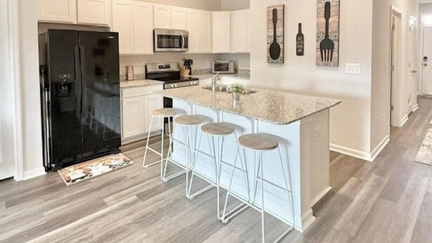 Una cocina moderna con armarios blancos, un refrigerador negro, un microondas y una isla central con taburetes.