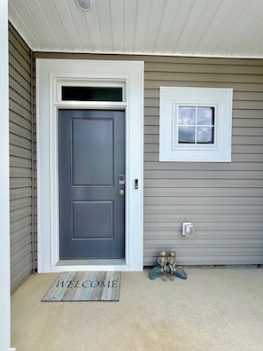 A front door with a 'WELCOME' mat, a small window above it, and a pair of decorative frogs on the ground. - NEW! Sweet Tee Beach Escape (Little River)
