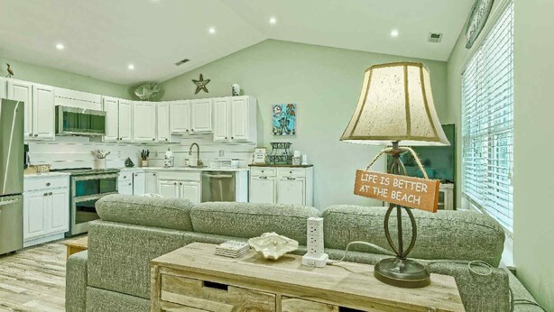Een woonkamer met een bank, een salontafel, een lamp en een keuken op de achtergrond.