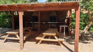En paviljong av trä med picknickbord och en grillplats.