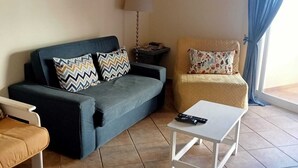 Un salon comprenant un canapé, un fauteuil, une table basse, une lampe et une fenêtre avec des rideaux.