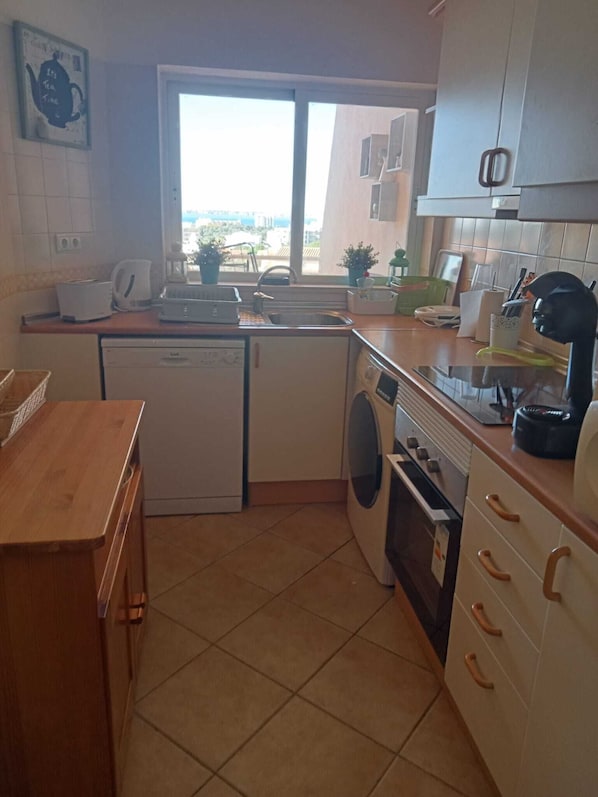 A compact kitchen with a dishwasher, washing machine, and a window providing a view of the outside.