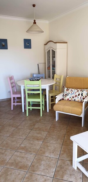 A dining area with a round table, chairs, a cabinet, and a sofa with a patterned cushion.