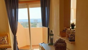 Un balcon avec vue, un canapé, une petite table, un meuble et une fenêtre avec des rideaux.