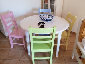 A round table with a bowl and sunglasses on it, surrounded by four chairs in different colors.