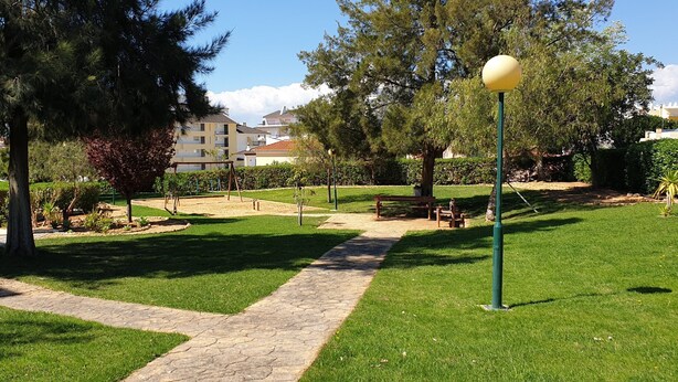 Un parc doté d’une allée pavée, de bancs et d’arbres.
