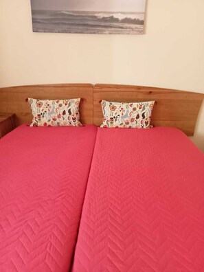 A double bed with a red quilt, two floral-patterned pillows, and a wooden headboard.