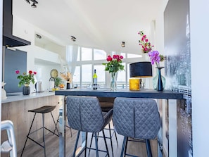 A modern kitchen with a bar area, two barstools, a cityscape view, and a large window. - Penthouse With Beach View (Sint-Annaland)