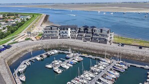 En lysthavn med flere både i havnen, en bygning med balkoner med udsigt over vandet og en sandstrand i baggrunden.
