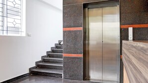 Un ascensor modern amb interior metàl·lic, al costat d'una escala de pedra granítica fosc amb accents taronja.