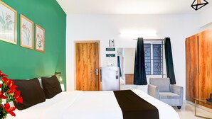 Habitació d'hotel amb un llit gran, un armari de fusta, una butaca grisa i una taula petita. Hi ha quadres amb marc a la paret i un senyal que indica que no es pot fumar a les habitacions.