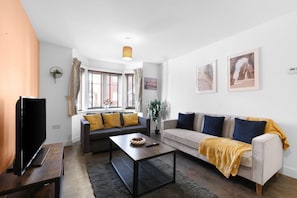 Ein Wohnzimmer mit einer Couch, einem Couchtisch, einem Fernseher und einem Fenster mit Vorhängen.