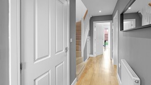 Un couloir avec des portes blanches, un plancher en bois, un escalier et un radiateur.