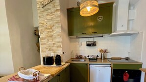 A compact kitchen with a stone accent wall, a hanging light fixture, and a built-in dishwasher. - La belle histoire du gîte Ventoux (Bédoin)