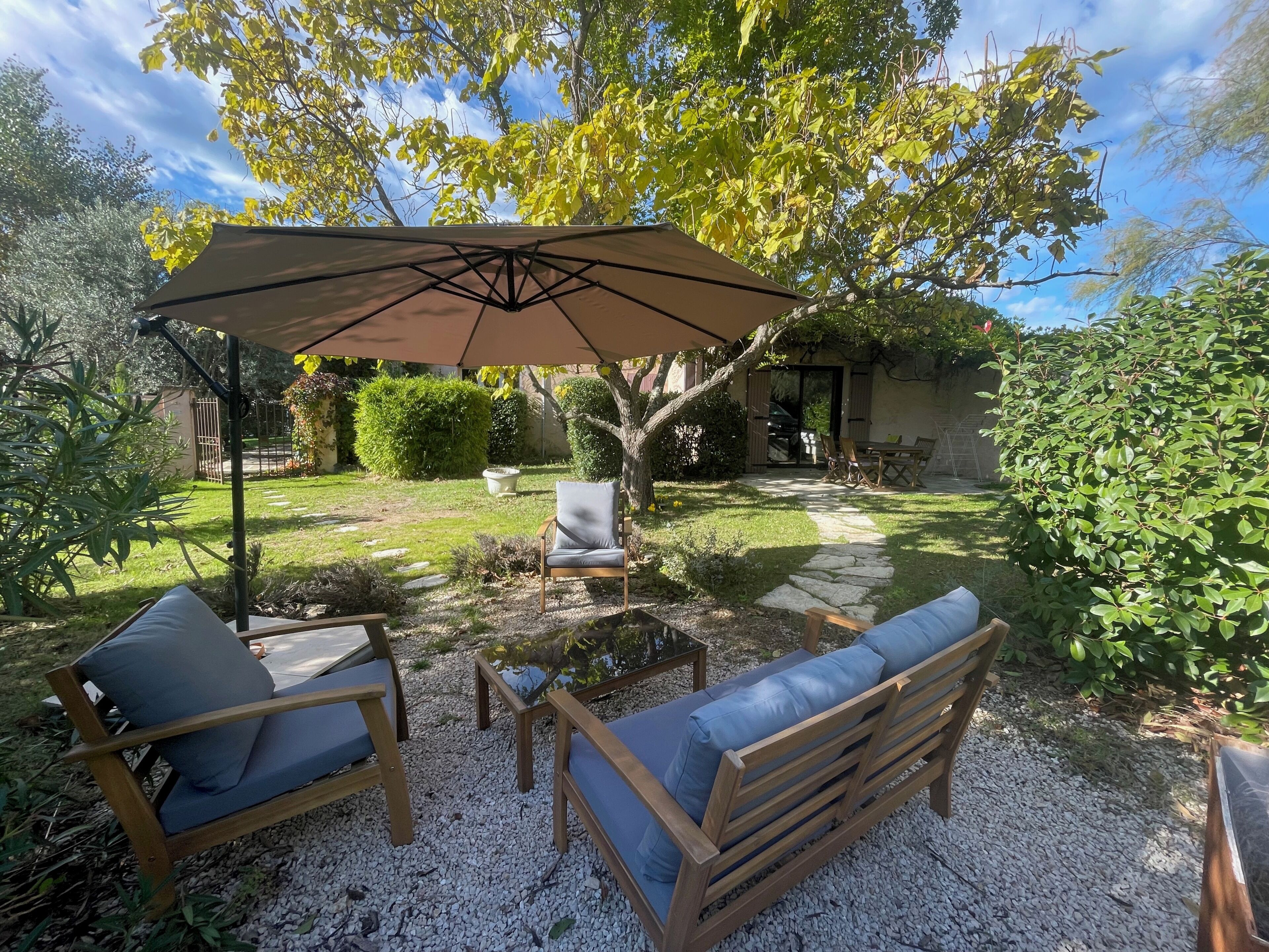 A patio with a table and two chairs, a large umbrella, and a tree.