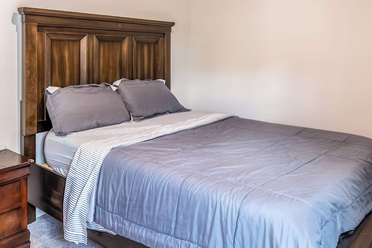 A neatly made bed with a wooden headboard, a striped blanket, and two pillows.