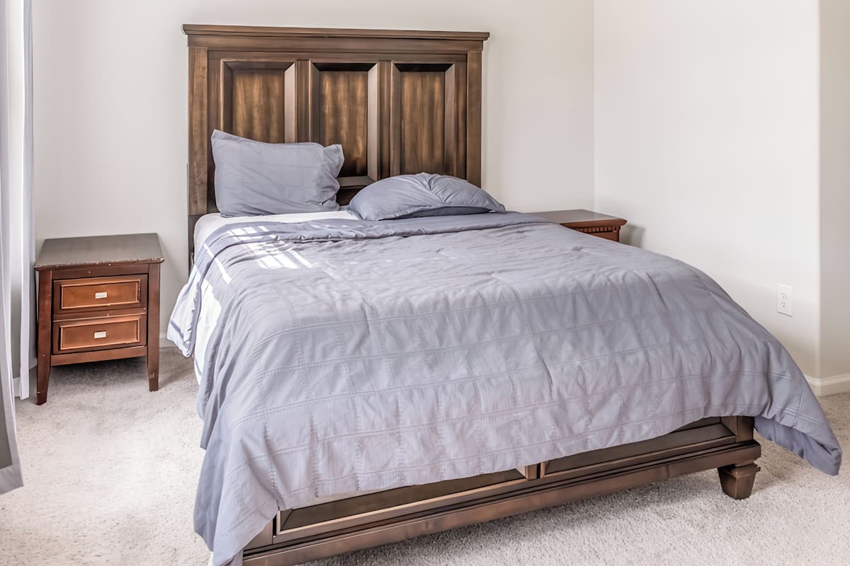 Un dormitorio con cama, dos mesitas de noche y cabecera de madera.