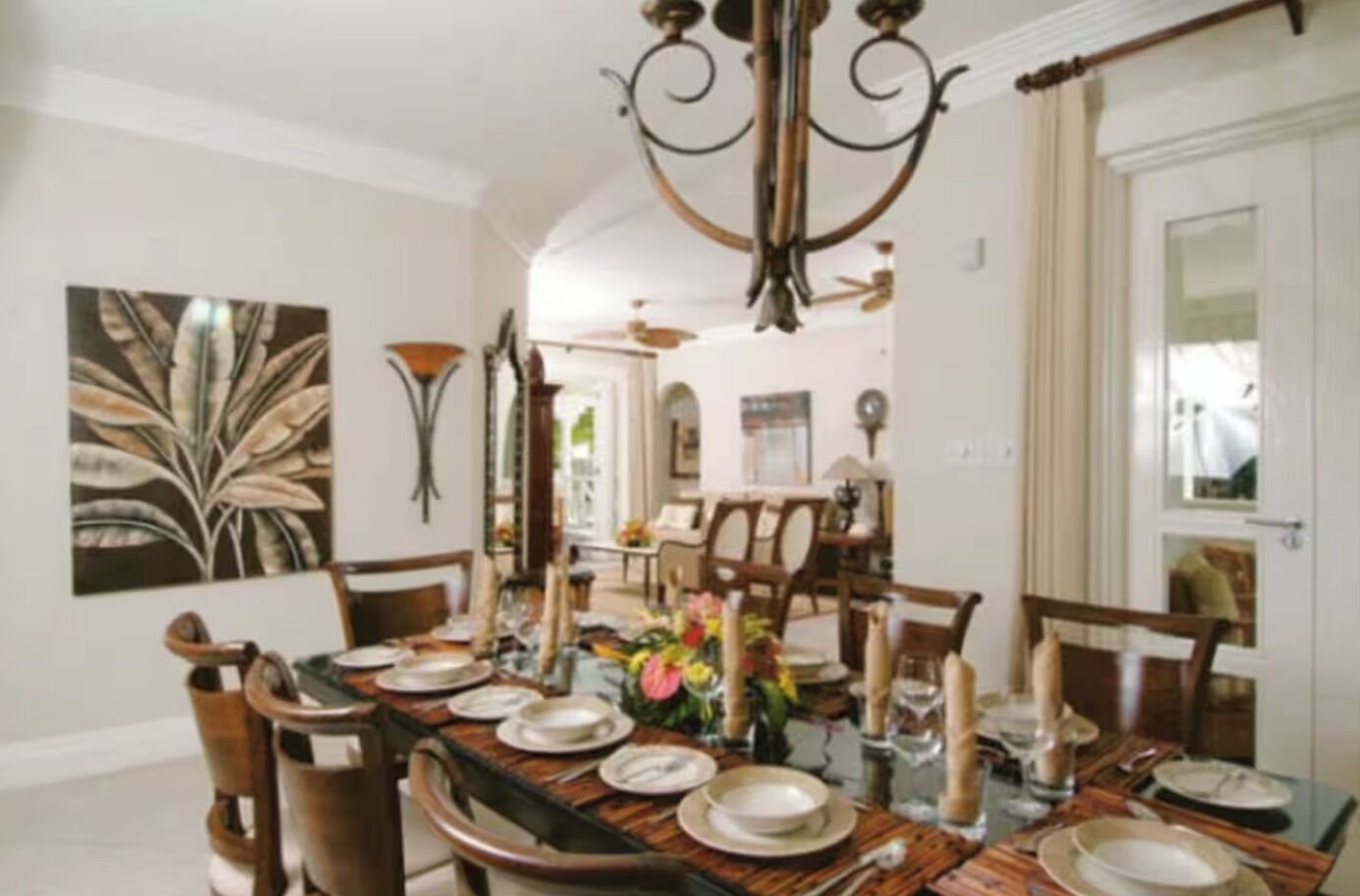 Une salle à manger avec une longue table dressée pour six personnes, entourée de chaises, et un lustre au-dessus.