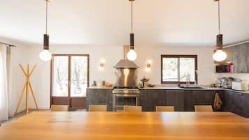 A modern kitchen with a central island, pendant lighting, and a large dining table.