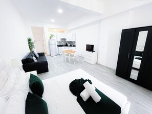 A modern hotel room with a bed, a sofa, a dining table, a TV, and a kitchen area. - DUCASSI SUITES STUDIOS HOTEL BEACH CLUB  (Punta Cana)