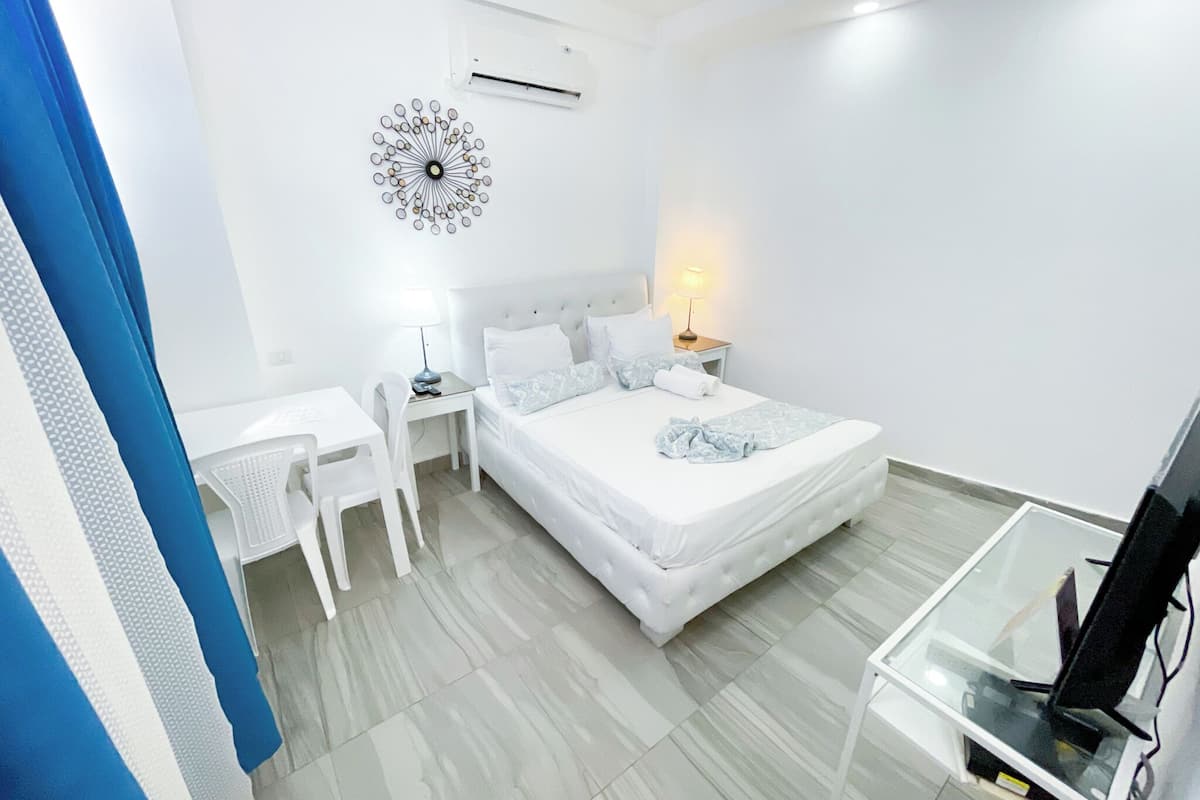 A bedroom with a bed, bedside table, lamp, and a desk with a chair.