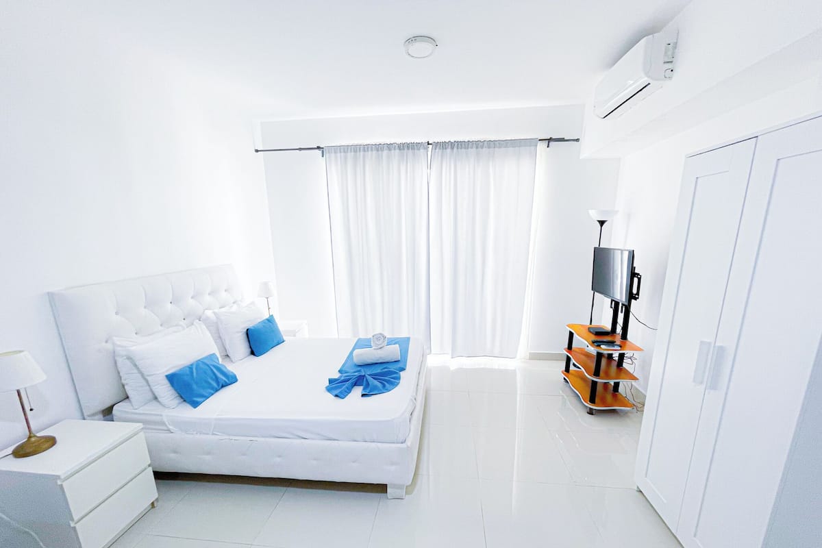 A hotel room with a bed, a TV, a wardrobe, and a window with curtains.