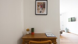Une pièce avec une table en bois, un tableau encadré au mur, un vase rempli de fleurs et un lampadaire.