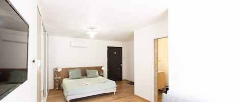 A bedroom with a bed, bedside lamps, a wooden floor, a door, and a mirror.